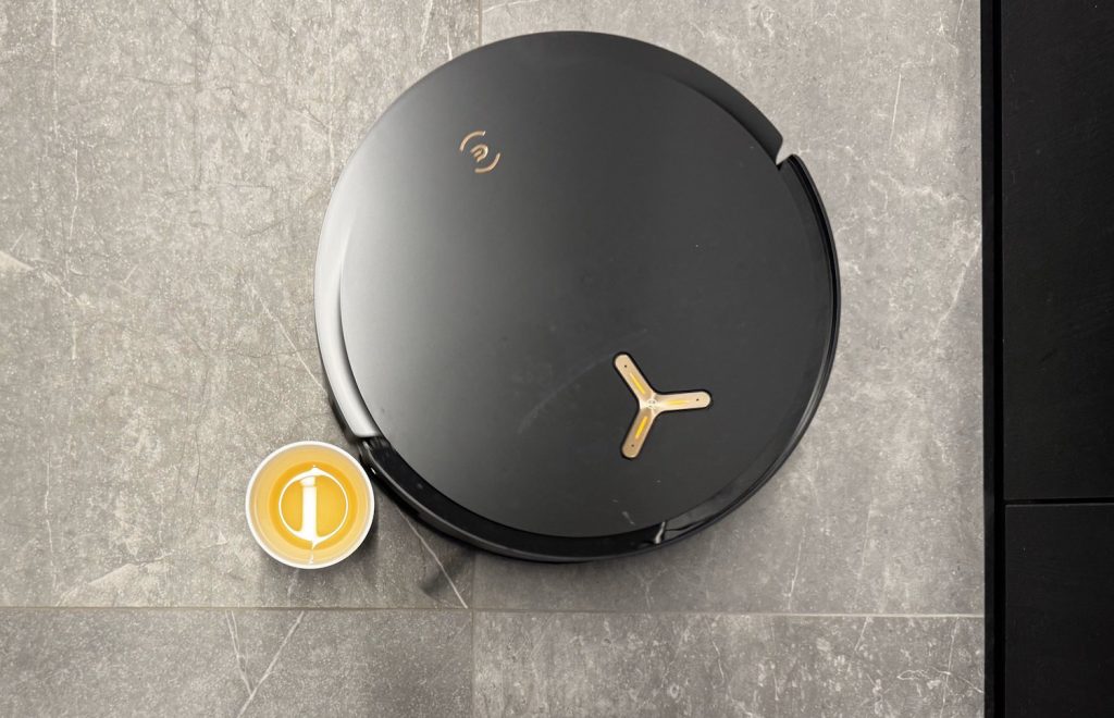 Top view of the Ecovacs Deebot X8 Pro Omni robot vacuum on a tiled floor next to a small cup of yellow liquid.