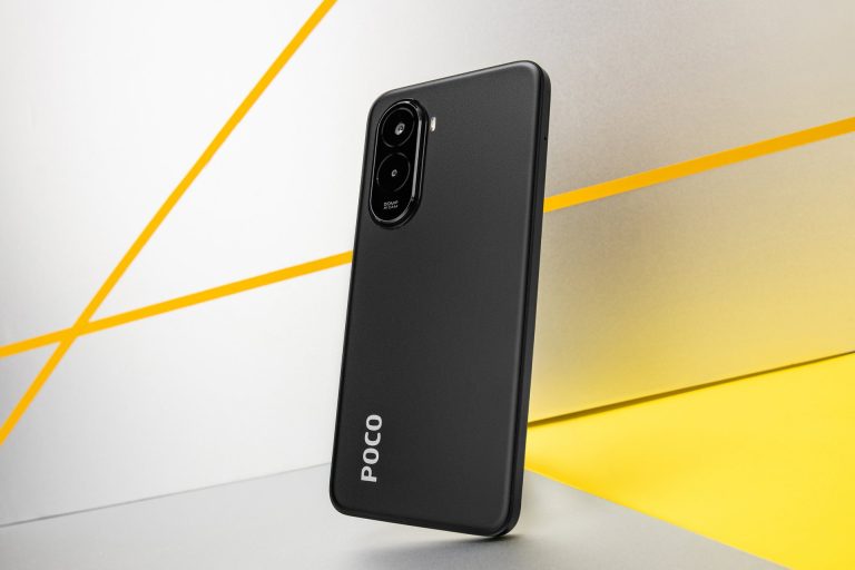A marketing shot of a black POCO smartphone resting at a slight angle on a surface. The phone is shown from the back, highlighting its matte finish, the vertical POCO logo at the bottom, and the black camera module with two large lenses. The background is a mix of white, gray, and yellow with two yellow diagonal stripes.