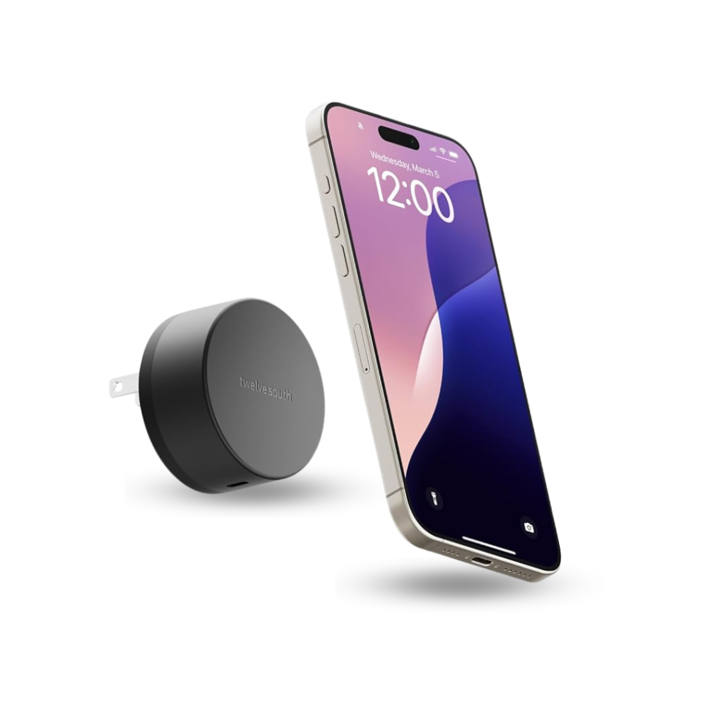 A product image of the "Twelve South PowerBug" wireless charger, shown alongside a smartphone. The charger is a small, matte black cylindrical puck with two foldable electrical prongs extending from its back. The "Twelve South" logo is subtly printed on the side. The charger is positioned to the left of a modern, light-colored smartphone which is floating and oriented vertically, displaying the lock screen with the time "12:00"